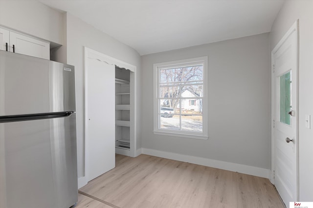 interior space with light wood finished floors, a closet, freestanding refrigerator, and baseboards