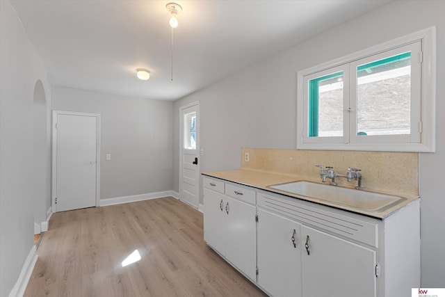 kitchen with arched walkways, a sink, white cabinetry, light countertops, and light wood-type flooring