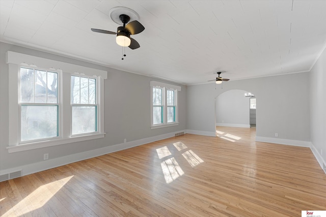 interior space featuring arched walkways, light wood-style flooring, visible vents, baseboards, and crown molding