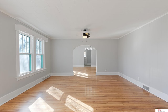 unfurnished room with ornamental molding, arched walkways, visible vents, and light wood-style flooring