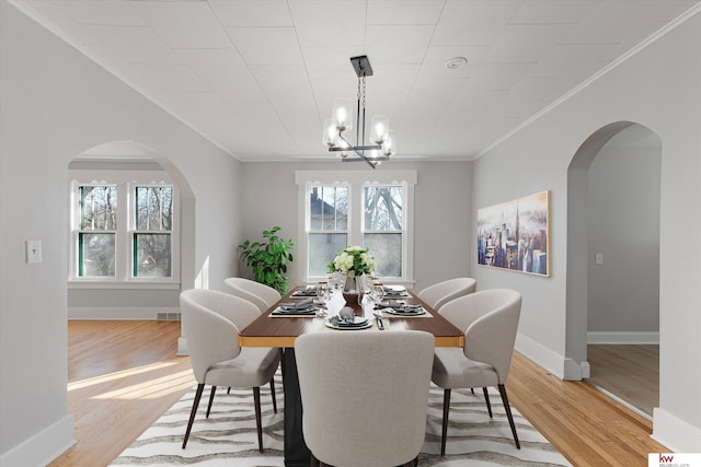 dining room with light wood finished floors, baseboards, arched walkways, an inviting chandelier, and crown molding