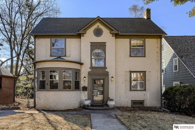 view of front facade with roof with shingles, a chimney, and stucco siding