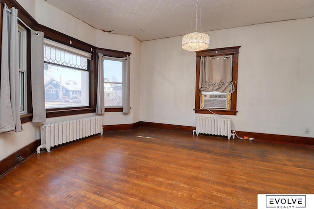 empty room with radiator, cooling unit, baseboards, and wood finished floors