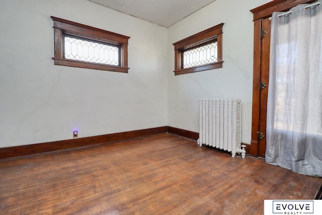 unfurnished room with baseboards, hardwood / wood-style floors, and radiator heating unit