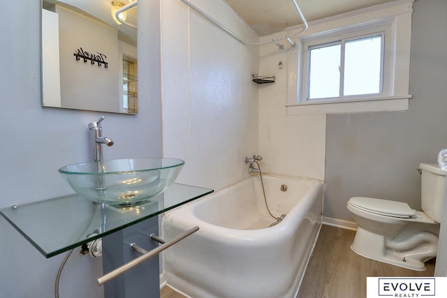 bathroom with baseboards, toilet, wood finished floors, washtub / shower combination, and a sink