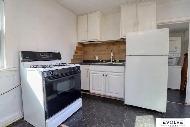 kitchen with dark countertops, freestanding refrigerator, stacked washing maching and dryer, a sink, and gas stove