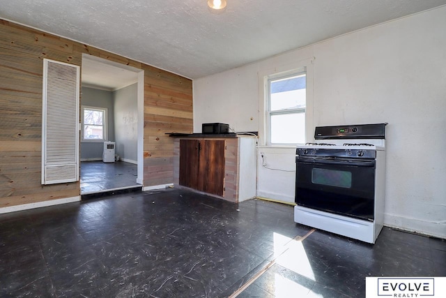 kitchen featuring range with gas cooktop, baseboards, wooden walls, and a textured ceiling