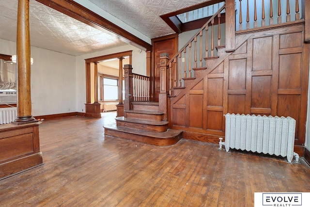 stairway featuring an ornate ceiling, radiator, and decorative columns