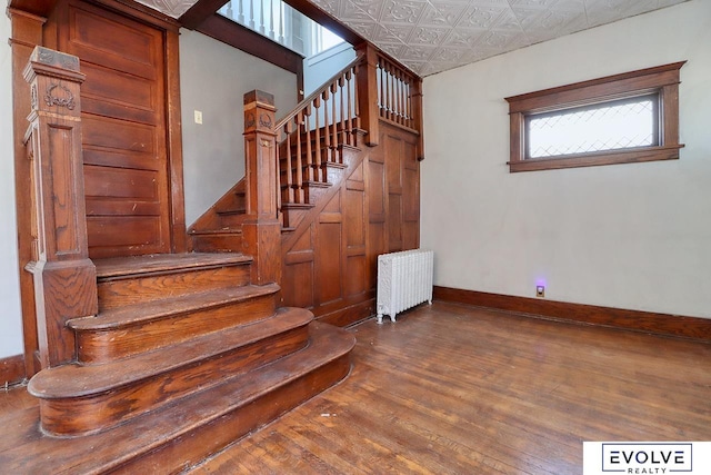 stairs with hardwood / wood-style flooring, an ornate ceiling, baseboards, and radiator heating unit