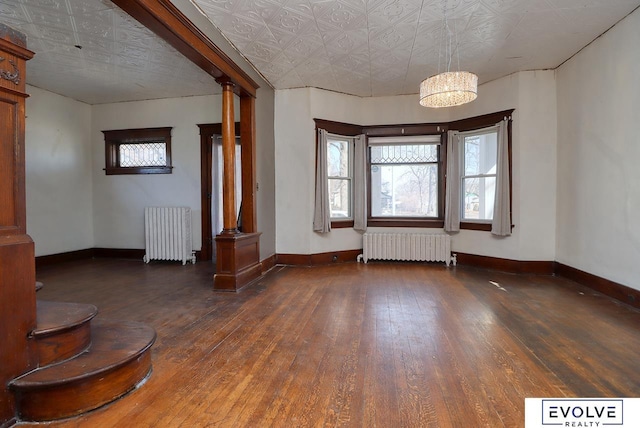 unfurnished room with radiator, ornate columns, radiator heating unit, and wood-type flooring