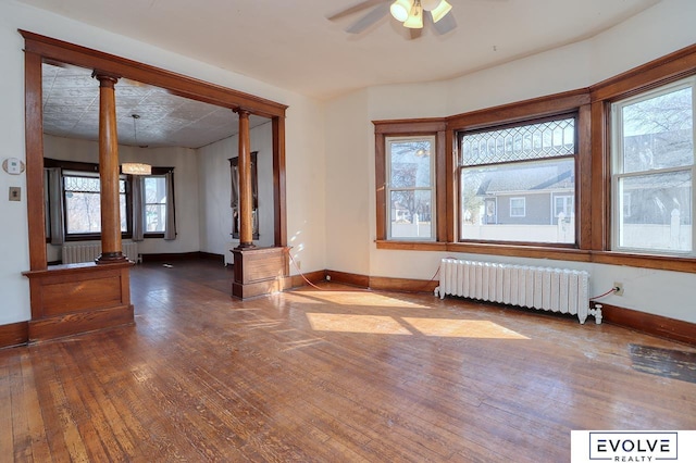 unfurnished room with baseboards, hardwood / wood-style flooring, decorative columns, and radiator