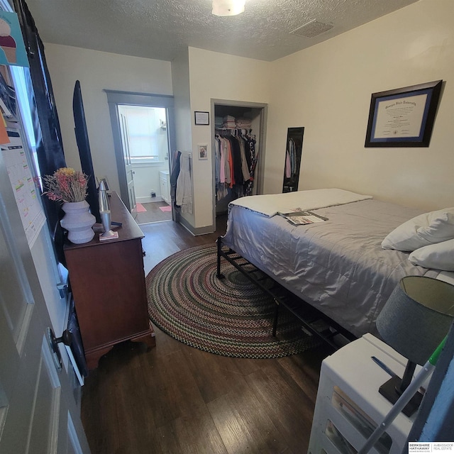 bedroom with a textured ceiling, a spacious closet, wood finished floors, and visible vents