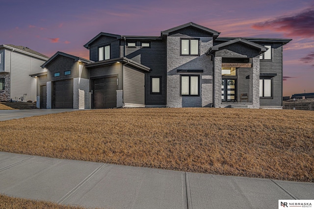 view of front of home with stone siding, an attached garage, concrete driveway, and a front lawn