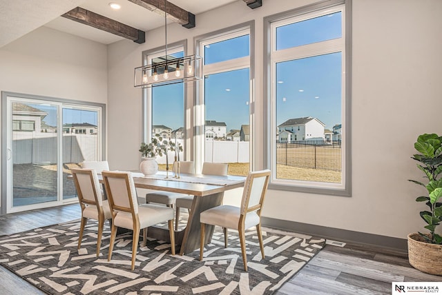 dining space featuring a notable chandelier, beamed ceiling, baseboards, and wood finished floors