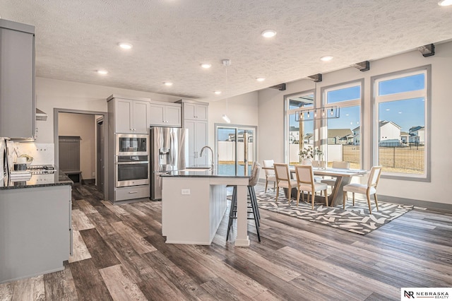 kitchen featuring a kitchen bar, dark wood-type flooring, a kitchen island with sink, a textured ceiling, and stainless steel appliances