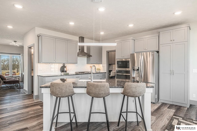 kitchen featuring dark wood-type flooring, appliances with stainless steel finishes, gray cabinetry, and wall chimney range hood