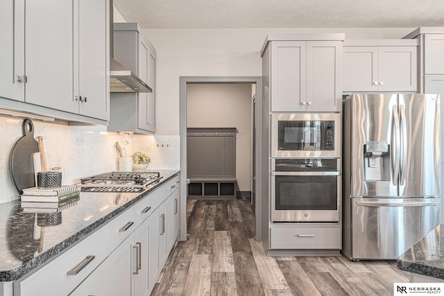 kitchen featuring decorative backsplash, dark stone countertops, appliances with stainless steel finishes, wood finished floors, and a textured ceiling