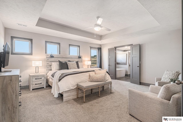 bedroom with a tray ceiling, multiple windows, light colored carpet, and visible vents