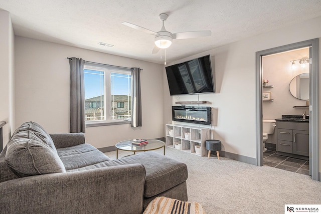 living room featuring visible vents, a ceiling fan, dark colored carpet, and a textured ceiling