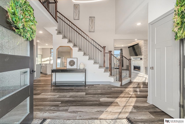 entryway featuring stairway, a warm lit fireplace, wood finished floors, and a towering ceiling