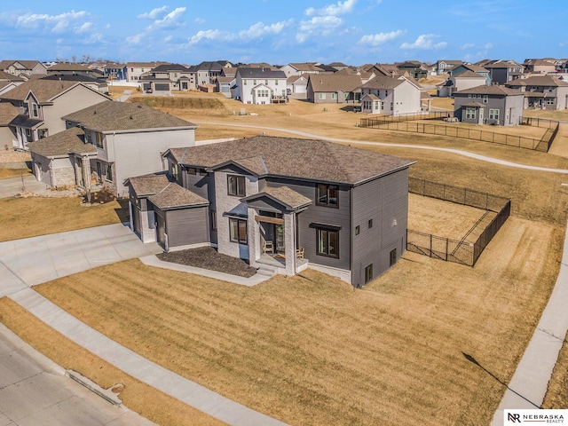 view of front facade with a residential view, concrete driveway, a front yard, and fence