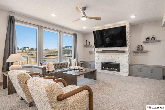 carpeted living area with a stone fireplace, recessed lighting, a textured ceiling, and ceiling fan