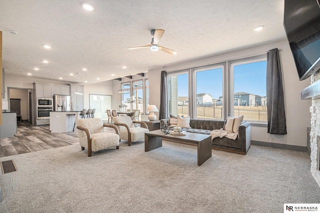 living room featuring recessed lighting, a ceiling fan, visible vents, and a textured ceiling