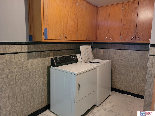 washroom with marble finish floor, tile walls, cabinet space, and washer and dryer