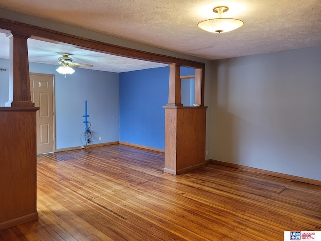 unfurnished room featuring decorative columns, baseboards, ceiling fan, hardwood / wood-style floors, and a textured ceiling