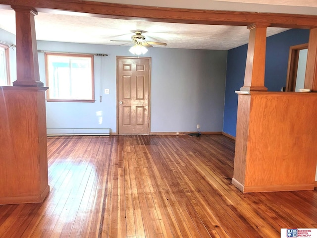 unfurnished living room with hardwood / wood-style floors, baseboard heating, decorative columns, and a ceiling fan