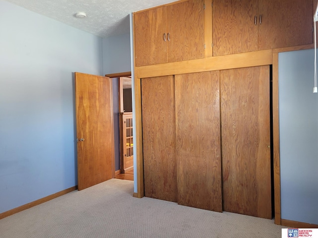 unfurnished bedroom featuring a textured ceiling, carpet floors, a closet, and baseboards