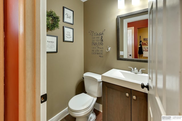 half bathroom with toilet, vanity, and baseboards