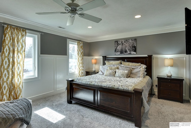 bedroom featuring visible vents, light colored carpet, ornamental molding, wainscoting, and a decorative wall