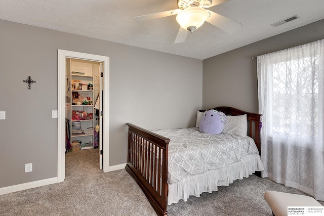 bedroom featuring visible vents, a walk in closet, carpet flooring, baseboards, and ceiling fan