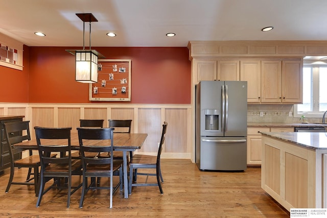 kitchen with light wood finished floors, wainscoting, decorative backsplash, stainless steel refrigerator with ice dispenser, and pendant lighting