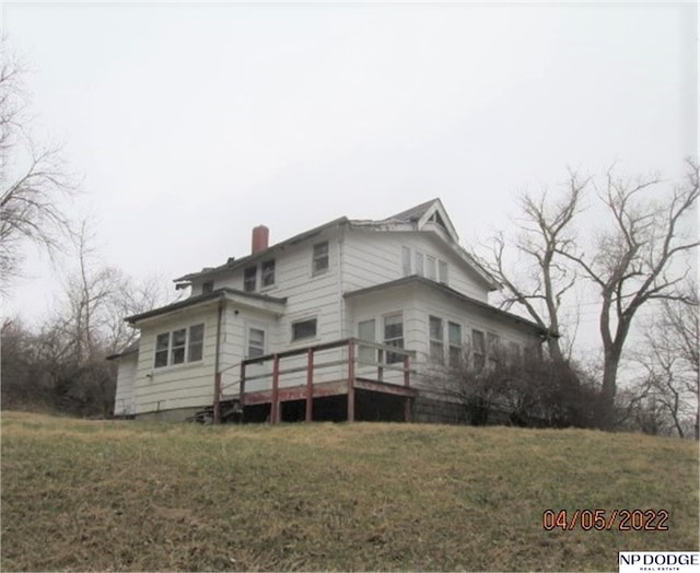 rear view of property featuring a chimney, a lawn, and a deck