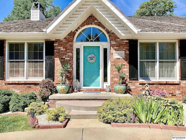 view of exterior entry featuring brick siding, roof with shingles, and a chimney