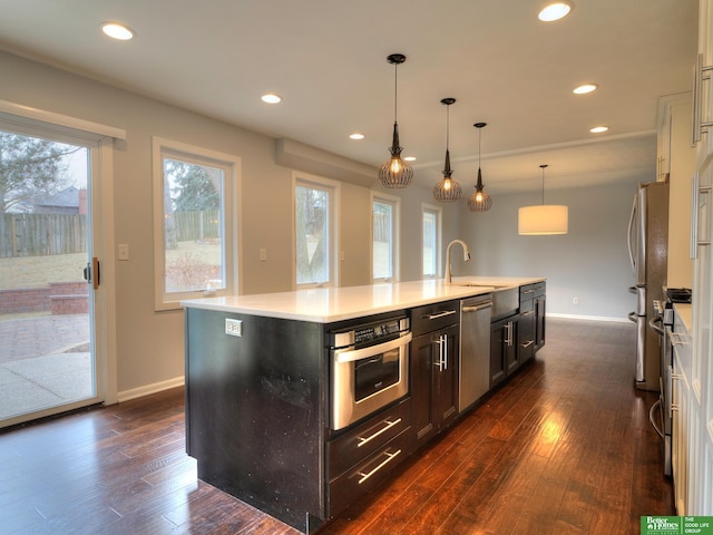 kitchen featuring an island with sink, dark wood finished floors, stainless steel appliances, and a sink