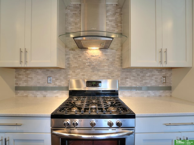 kitchen with wall chimney exhaust hood, stainless steel gas range oven, white cabinetry, and tasteful backsplash