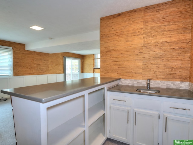 kitchen with decorative backsplash, white cabinets, wainscoting, a peninsula, and a sink