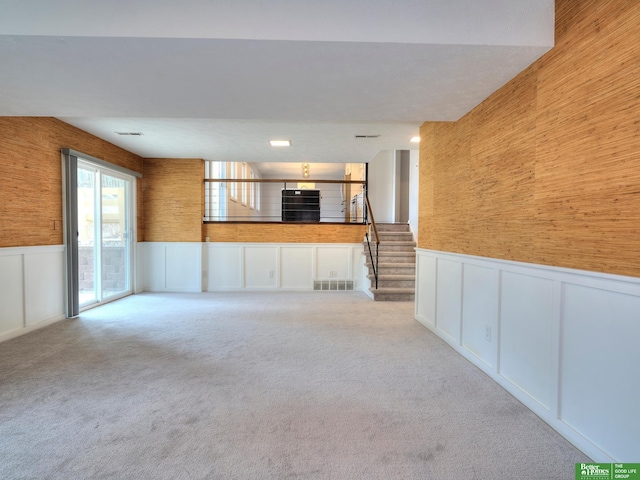 unfurnished living room with light carpet, a wainscoted wall, and visible vents