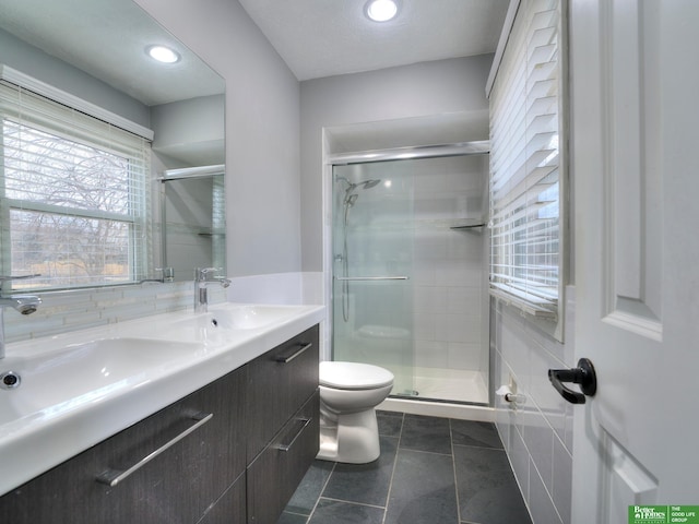 bathroom with double vanity, a stall shower, a sink, and toilet