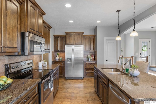 kitchen featuring dark stone countertops, appliances with stainless steel finishes, light wood-style flooring, and a sink