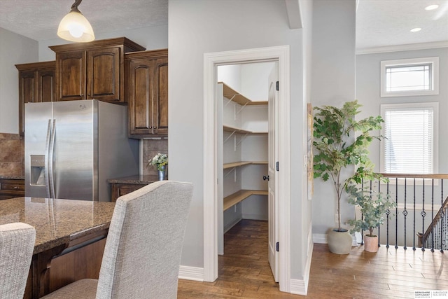 kitchen featuring wood finished floors, baseboards, tasteful backsplash, dark stone countertops, and stainless steel fridge