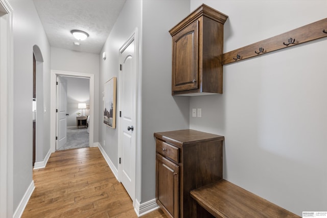 hall with light wood finished floors, baseboards, arched walkways, and a textured ceiling