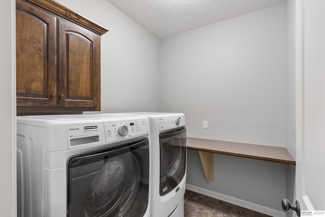 clothes washing area with a textured ceiling, washer and clothes dryer, cabinet space, and baseboards