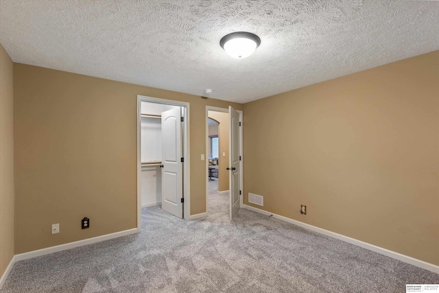 unfurnished bedroom featuring carpet, a walk in closet, a closet, visible vents, and baseboards