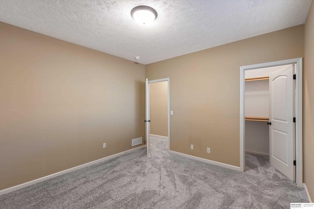 unfurnished bedroom with a textured ceiling, carpet floors, visible vents, baseboards, and a spacious closet