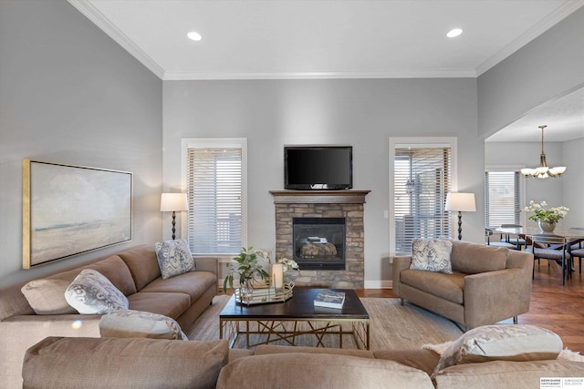 living room with a chandelier, crown molding, a stone fireplace, and wood finished floors