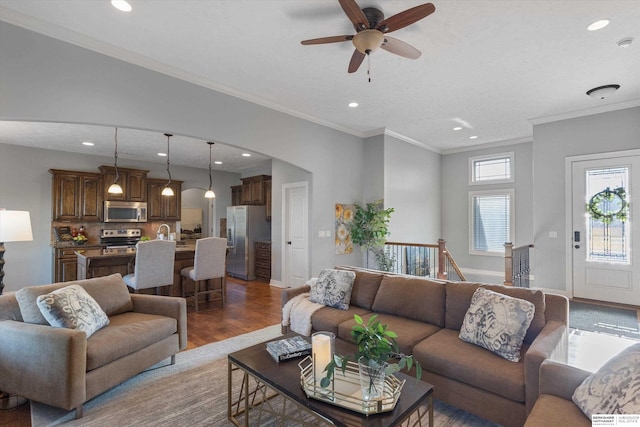 living room featuring arched walkways, recessed lighting, ornamental molding, wood finished floors, and baseboards